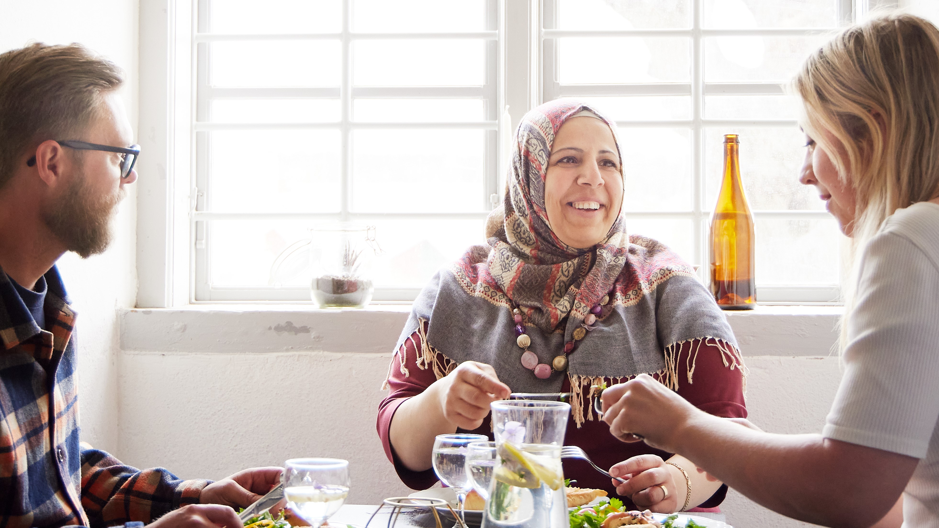 tre glada personer som sitter vid ett bord och äter och pratar