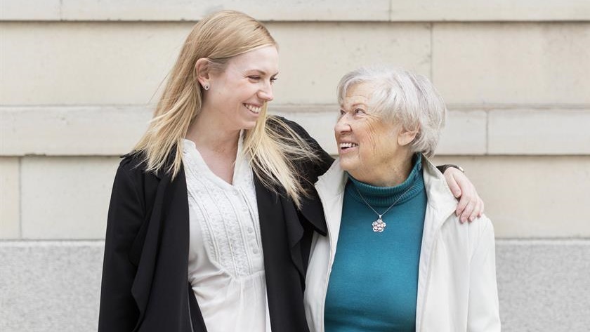 En yngre person och en äldre person står bredvid varandra, tittar på varandra och är glada En yngre person och en äldre person står bredvid varandra, tittar på varandra och är glada