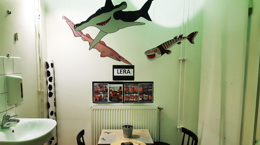 Ett av rummen med bord och stolar, fiskar i taket och en skylt där det står lera
