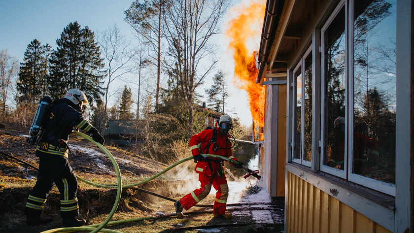 Ett hus som brinner och två brandmän med en slang